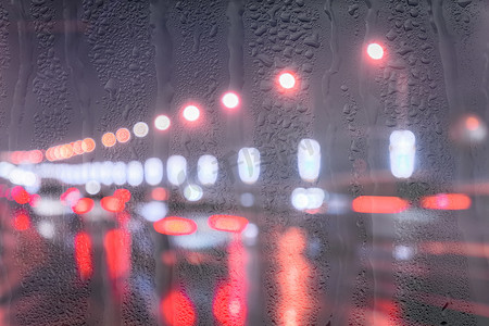 行驶中的汽车和灯笼的模糊灯光反射在夜城被雨覆盖的窗户后面潮湿的沥青上。