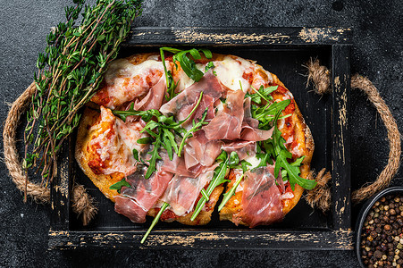 托木尔摄影照片_意大利披萨配火腿帕尔马火腿、芝麻菜沙拉和奶酪，装在质朴的木托盘中。