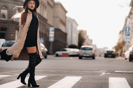 城市街道上穿着米色外套、戴着黑帽子的时尚年轻女子。