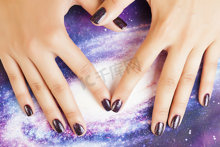 美甲时尚概念：指甲上有紫色闪光的女性手指，如宇宙、宇宙背景