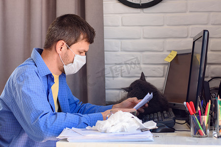 一个戴着医用口罩的男子在远程工作时阅读文件