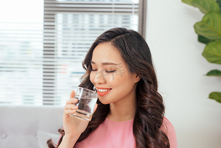年轻美丽的亚洲女性在沙发上放松，喝着一杯纯净水
