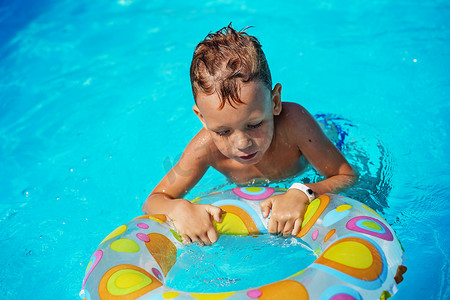 游泳圈的男孩摄影照片_快乐的孩子在游泳池蓝色的水中玩耍。