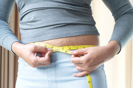 胖女人手拿着测量卷尺测量她的腹部脂肪。
