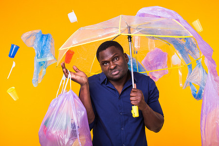 垃圾、塑料回收、污染和环境概念问题 — 黄色背景下携带垃圾袋的困惑男子
