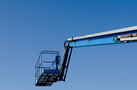 安全电梯安全摄影照片_伸缩臂升降机在蓝天背景下升起，运送到施工现场，准备供钢架安装工、屋顶工和油漆工使用