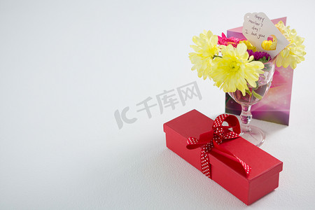 礼盒和玻璃杯中的鲜花，上面贴着母亲节快乐的标签