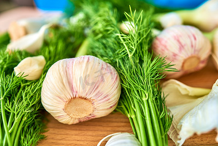 新鲜蒜头摄影照片_切菜板上放着几颗新鲜大蒜头和几瓣，周围是莳萝。