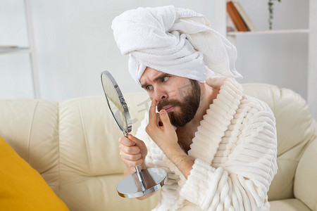 皮肤斑点摄影照片_留着胡子的男人检查他脸上的皮肤。