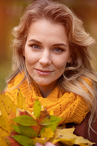 年轻迷人的女人摆着落黄的叶子拍照，在秋黄的花园或公园里散步。