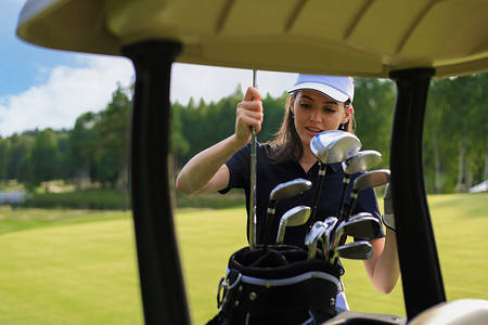 游戏礼包盒摄影照片_职业女子高尔夫球手从包里选择高尔夫球杆。