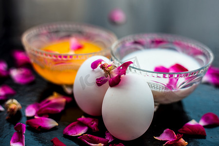 抗衰老面膜，即牛奶和鸡蛋面膜，装在玻璃碗中，表面呈闪亮的黑色，上面有一些玫瑰花瓣及其全部成分。