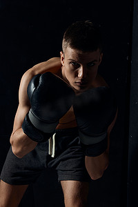 中的战斗机摄影照片_戴着黑色手套的拳击手在深色背景健美健身锻炼中弯下腰