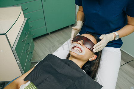 女顾客摄影照片_一家诊所的女顾客张着嘴坐在牙科椅上，戴着橙色安全眼镜。