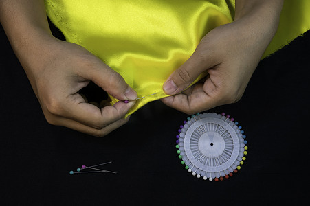 黑色别针摄影照片_亚洲女性的特写手在黑色背景上缝纫前用别针缝合。