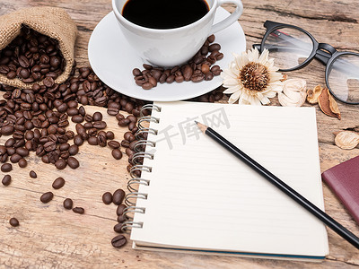 热咖啡杯加咖啡豆和笔记本用木制的桌子上的铅笔。