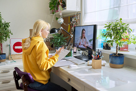 十几岁的女孩坐在家里使用家用电脑在线学习。