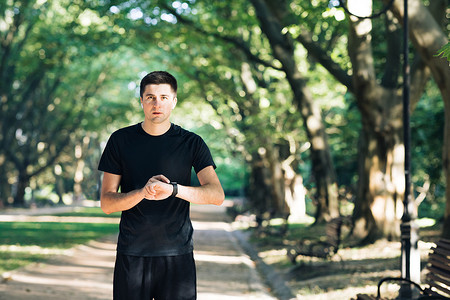 成年男子使用无线蓝牙耳机在户外跑步，用智能手表听音乐，享受健康。
