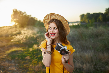 烈焰红唇摄影照片_手里拿着相机的漂亮女人在大自然中看着侧面微笑红唇夏天