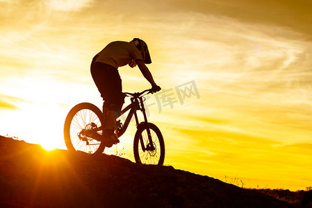 日落时骑自行车者在落基山上骑山地自行车的剪影。