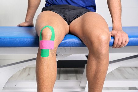 年轻的运动男运动员用肌内效胶带治疗受伤的膝盖。