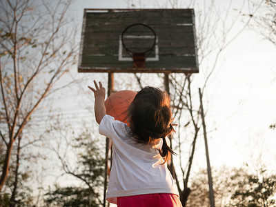 可爱的亚洲小孩在夏季的操场上打篮球。