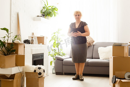 自由摄影照片_快乐兴奋的成熟退休中年女性独自站在现代客厅内部，张开双臂享受自由和幸福，对新装修的家居概念感到动力