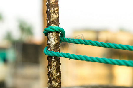 一根绳子在栅栏柱周围打结，绳子在与背景隔离的生锈铁杆上打结。
