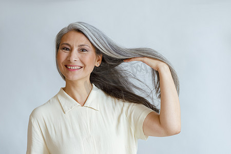 快乐的中年亚洲女士在浅色背景下展示自然的银发