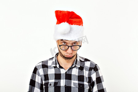 圣诞老人胡子帽子摄影照片_一个有趣的年轻人的肖像，戴着圣诞老人帽子，留着白色背景的胡子。