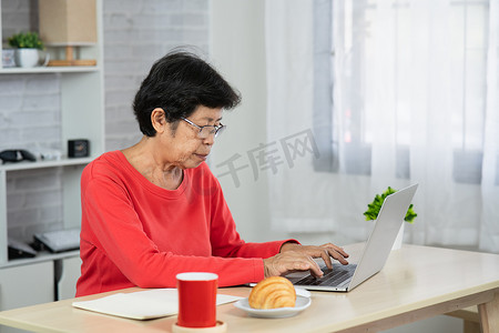 室内家居平面摄影照片_高级亚洲女性坐在桌子上使用笔记本电脑放松。
