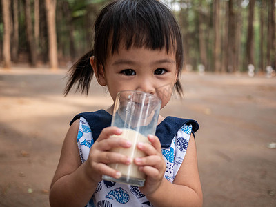 亚洲小孩在花园里喝着玻璃杯里的牛奶，味道鲜美。