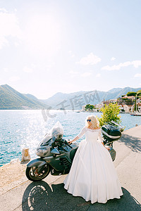 双人结婚登记照摄影照片_佩拉斯特老城码头上，一位戴着墨镜、身穿婚纱的新娘站在摩托车旁