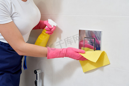 手戴着橡胶防护手套清洁厕所冲水按钮。