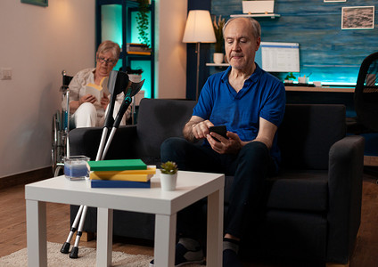 退休男子坐在家里的沙发上使用智能手机