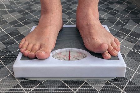 一名年轻人赤脚在体重秤上称重，以控制体重并遵循饮食习惯