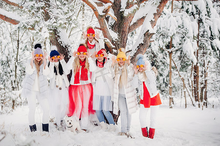 白雪皑皑的森林摄影照片_一大群拿着橘子的女孩站在冬天的森林里。白雪皑皑的森林里，穿着红色和白色衣服、带着水果的女孩