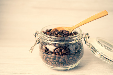 饮料食品摄影照片_玻璃罐瓶中的咖啡豆，配有木勺，新鲜饮料食品早晨。
