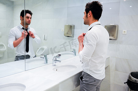 公共洗手间摄影照片_男子在带镜子的公共卫生间穿衣服