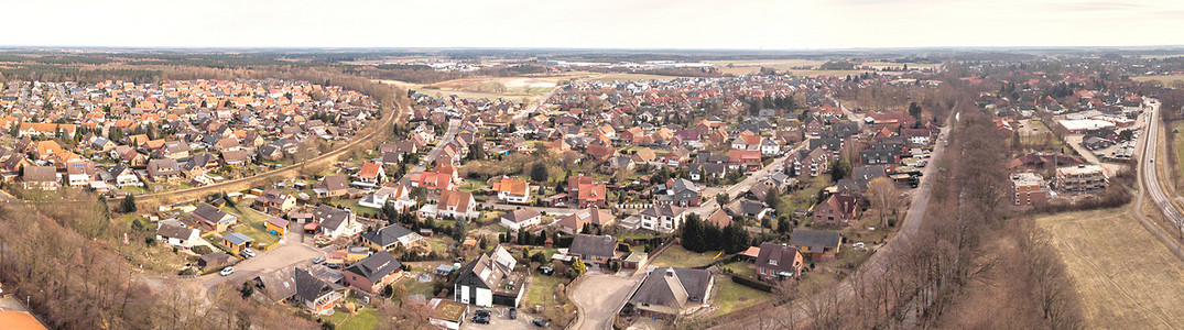 德国北部荒原上的一个小村庄的空中照片和空中照片的合成全景图，屋顶上方有草地、田野和房屋。