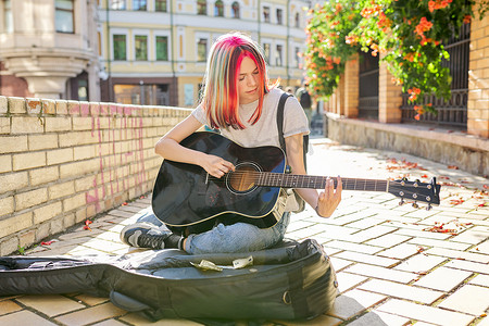 坐在人行道上弹吉他的创意女性，带着吉他盒和现金