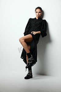 身穿黑色连衣裙、妆容鲜艳的黑发美女将腿弯曲在膝盖处