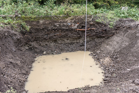 挖坑摄影照片_有地下水入口和测量杆​​的开挖坑