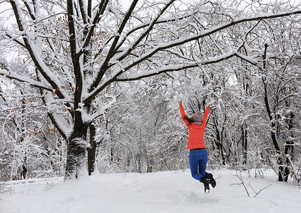 冬天，年轻漂亮的女孩在多枝多年生老橡树附近的白雪覆盖的童话森林里散步，快乐地跳跃