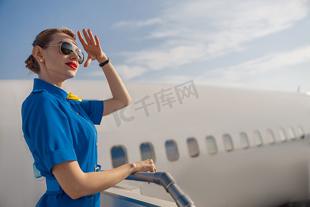 白天，身着蓝色制服、戴着墨镜、手握着头、看着远处的优雅空姐的肖像