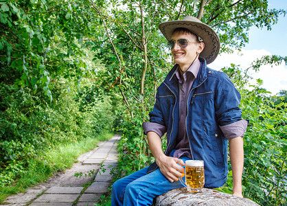 牛仔喝酒摄影照片_牛仔帽和太阳镜的年轻人正在喝啤酒