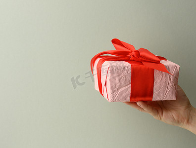 女手拿着灰色背景的粉色礼盒，生日快乐的概念