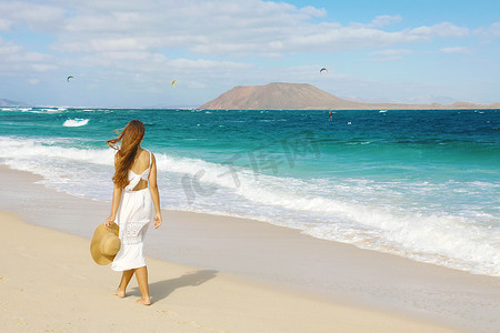 在加那利群岛富埃特文图拉岛科拉莱霍野生海滩上行走的年轻女子，看着背景中的洛博斯岛