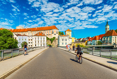 云南过桥米线菜单摄影照片_施泰尔 — 2020年6月，奥地利：一名男子骑着自行车过桥，前往美丽的奥地利城市施泰尔的中心