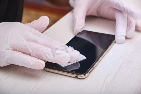 一名戴着橡胶手套的男子用湿布擦拭智能手机的玻璃，然后粘上防护玻璃